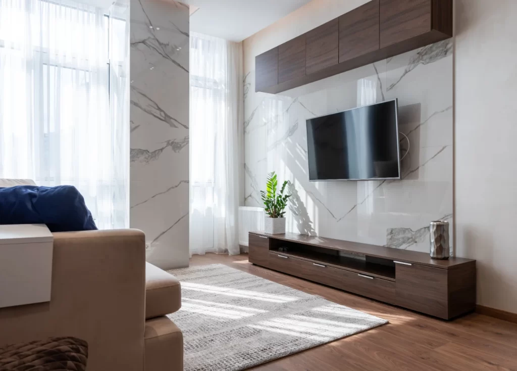Home Remodeling Modern living room with marble accent wall, floating TV stand, natural light, and minimalist decor for a clean and elegant design.