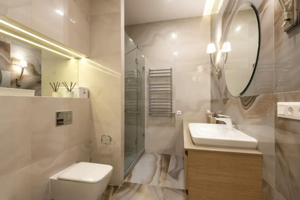 Modern bathroom remodeling with marble accents, minimalist vanity, round mirror, and glass shower enclosure for a contemporary design.