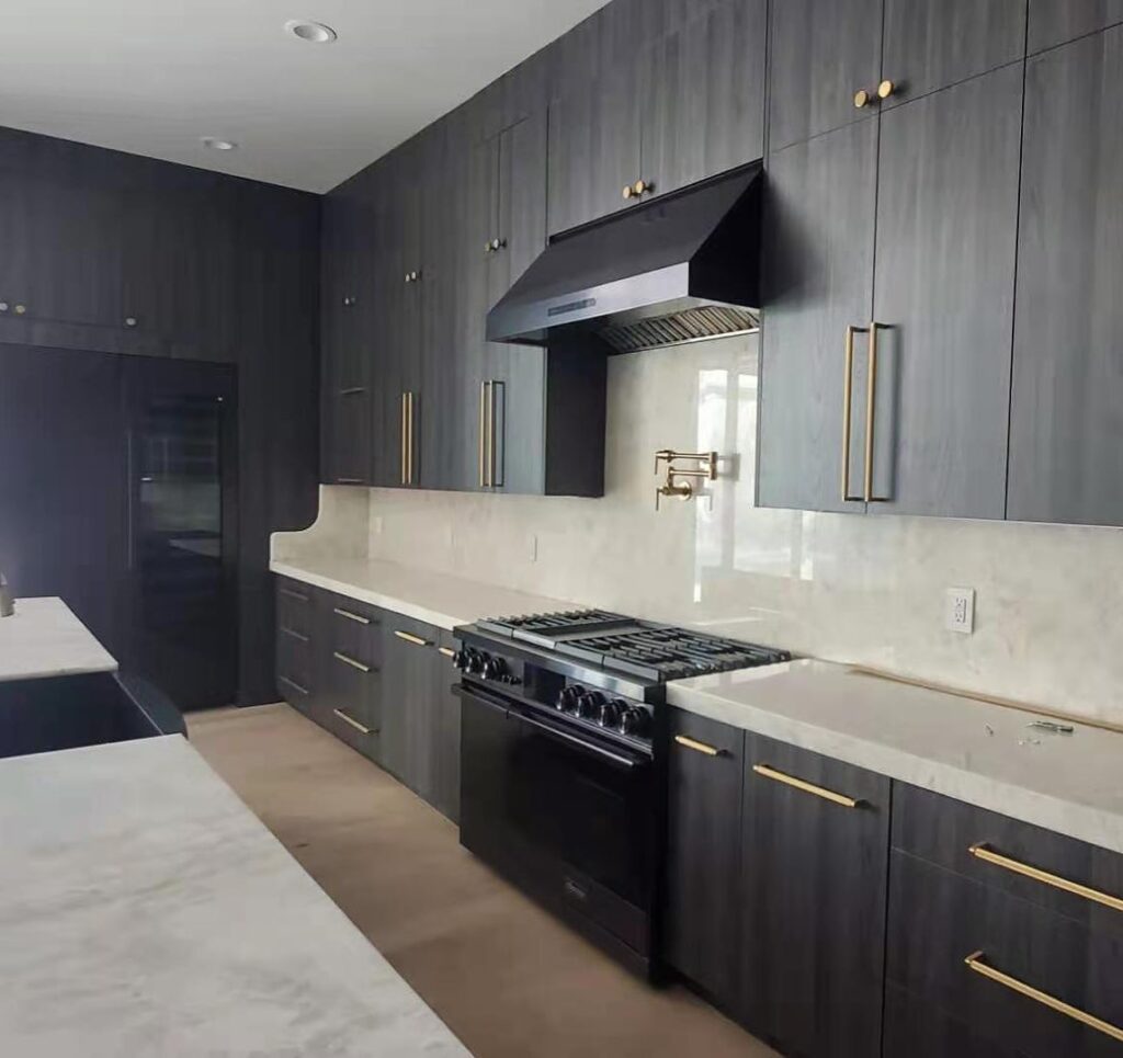 Modern kitchen remodeling design with dark cabinets, marble countertops, sleek black appliances, and brass hardware for a sophisticated look.