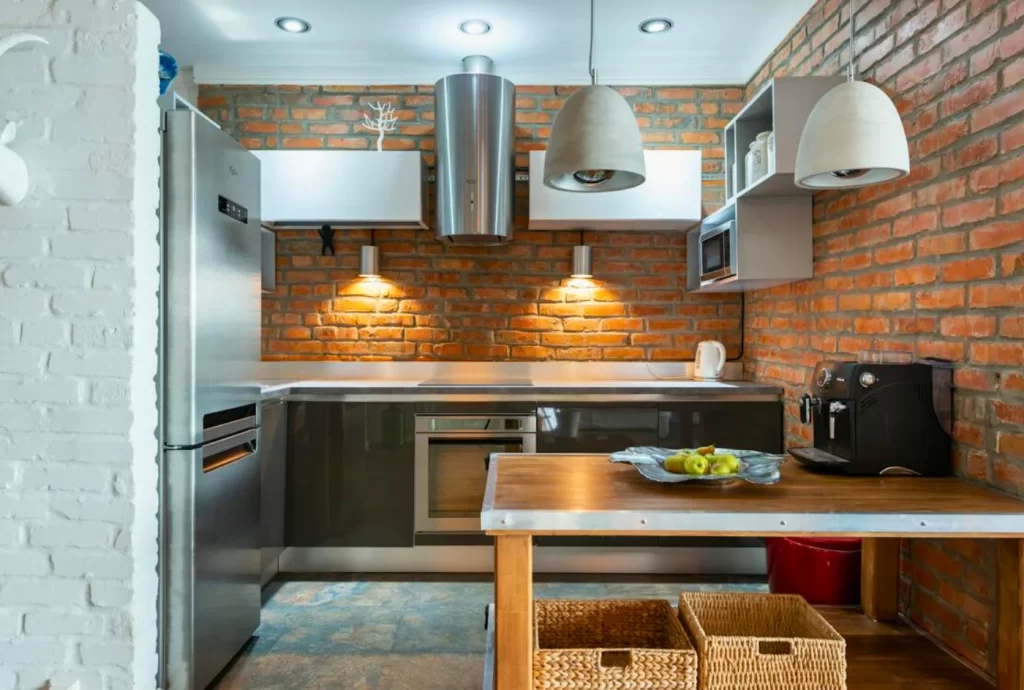 Industrial kitchen remodeling design with exposed brick wall, stainless steel appliances, open shelving, and pendant lighting for a modern rustic look.