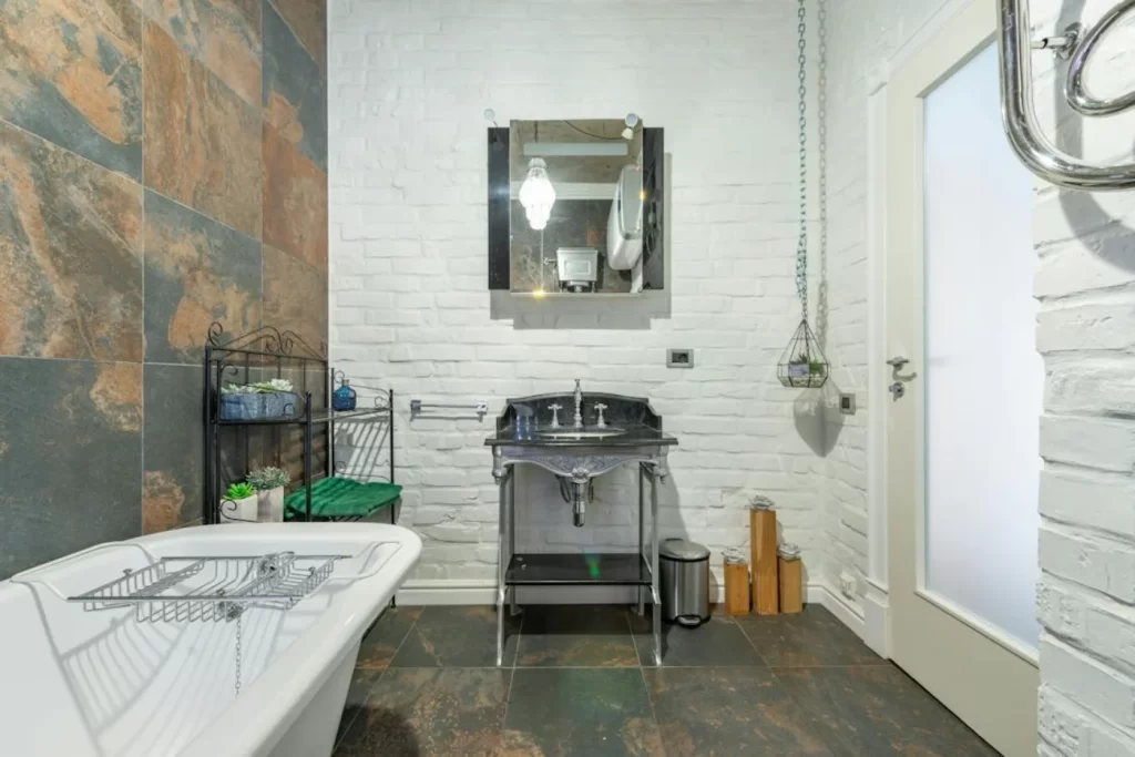 Industrial-style bathroom remodeling with exposed brick wall, freestanding tub, and rustic metal sink vanity.
