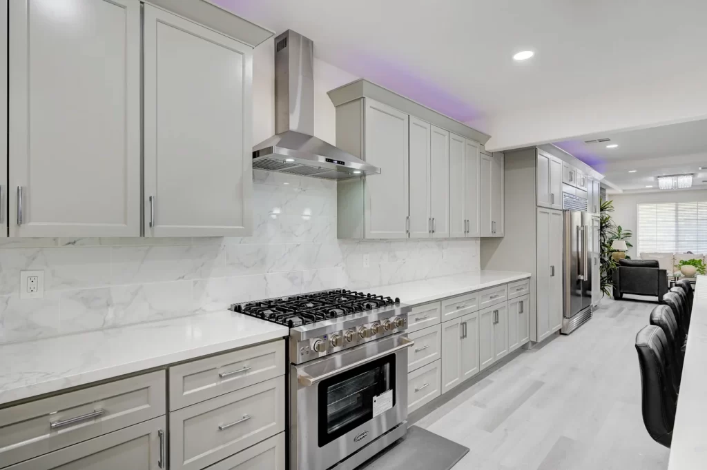 Modern kitchen remodeling with light gray cabinets, stainless steel appliances, and white marble backsplash.